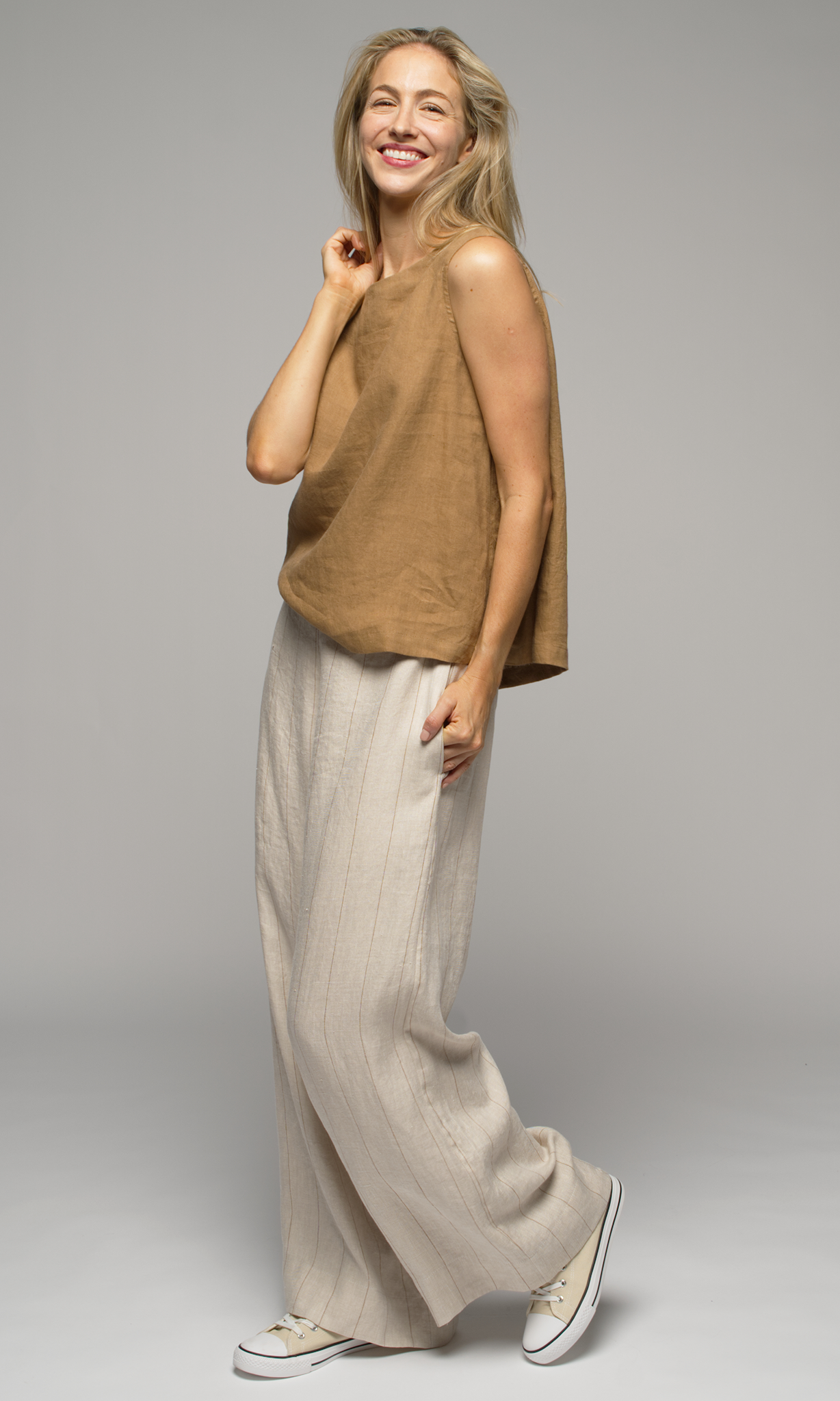 Woman wearing a brown sleeveless top and beige striped pants.