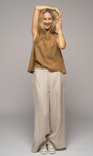 Woman wearing a brown sleeveless top and beige striped pants, arms over her head.