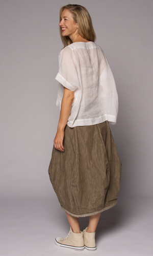 Blonde woman modelling a white linen top with a brown loose skirt, showing us her back.