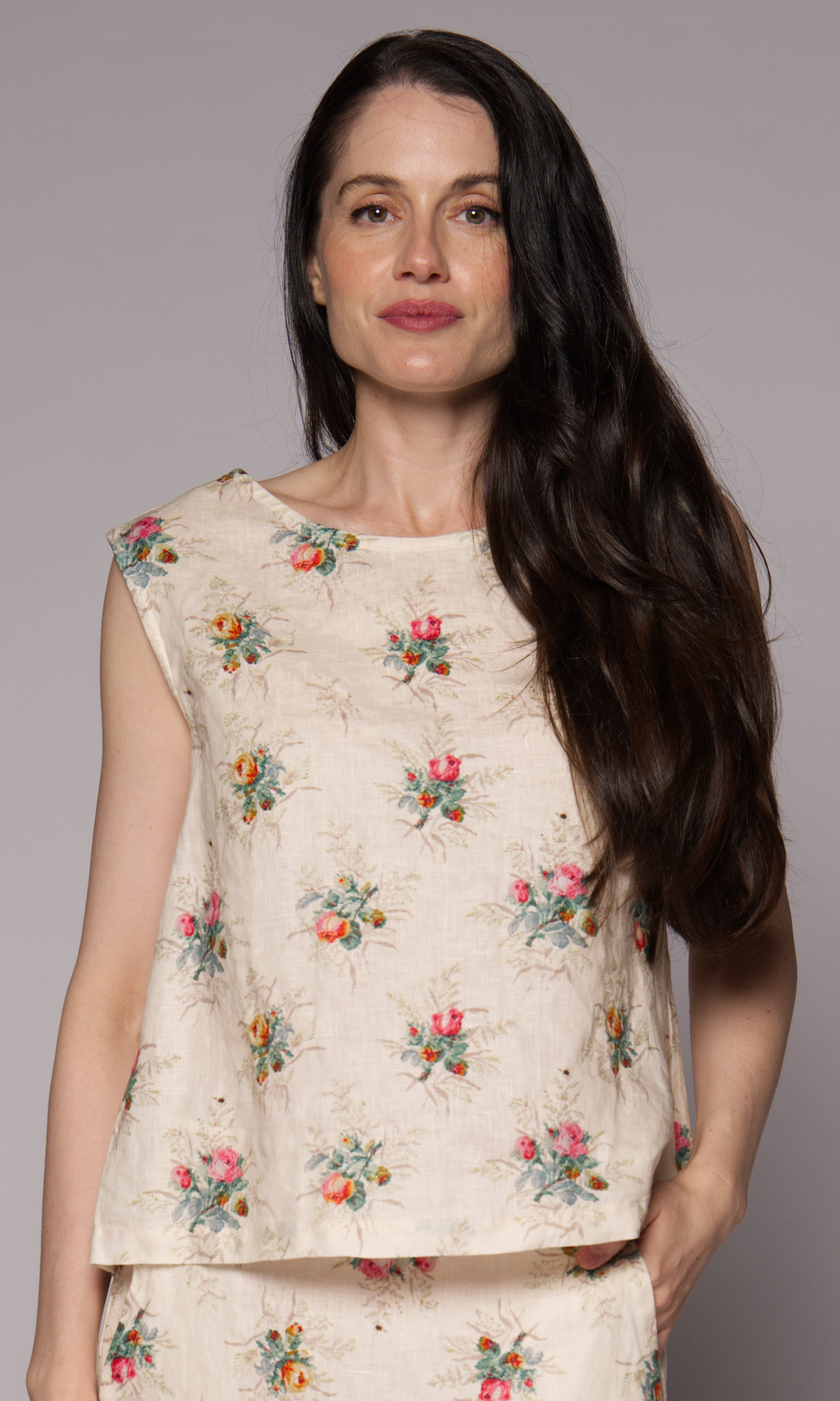 Close-up of a dark-haired woman in a cream floral singlet top and matching skirt.