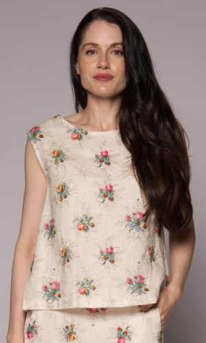 Close-up of a dark-haired woman in a cream floral singlet top and matching skirt.