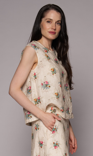 Side view of a dark-haired woman in a cream floral singlet top and matching skirt, showing pocket detail.