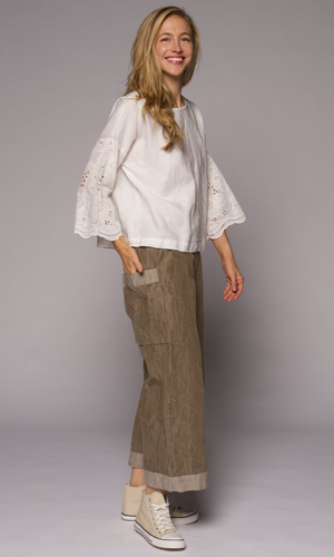 Blonde woman models white top with brown denim pants, showing her side with the wrap-around pocket visible.