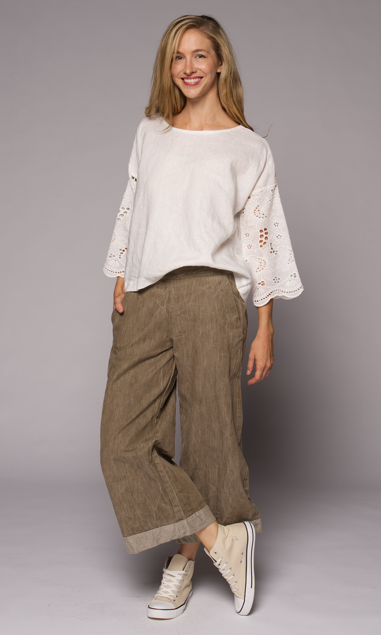 Blonde woman models white top with brown denim pants, showing facing camera with the wrap-around pocket visible.