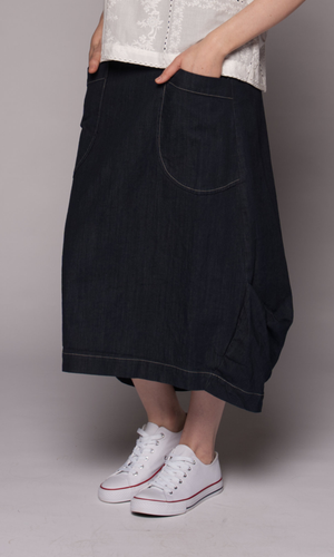 A person wearing a dark indigo denim midi skirt with front patch pockets, paired with a white lace-trim top and white low-top sneakers.