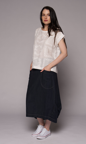 A woman modelling a white short-sleeve cropped knit top with eyelet embroidery and a dark navy wide-leg denim skirt, paired with white sneakers.