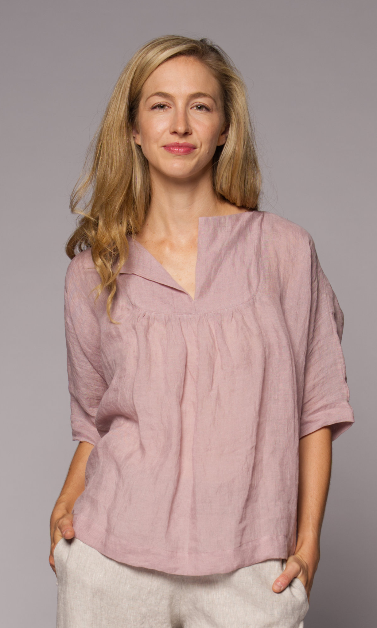 Blonde haired woman modelling a light pink linen top and linen pants with hand in pocket.