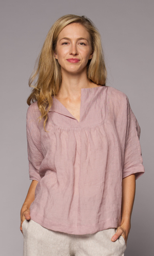 Blonde haired woman modelling a light pink linen top and linen pants with hand in pocket.