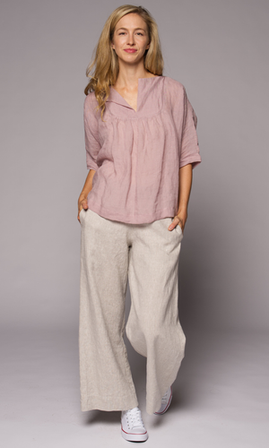 Blonde haired woman modelling a light pink linen top and linen pants with hand in pocket.