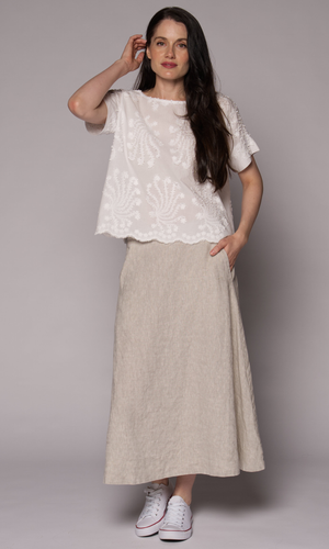 Dark brown haired woman modelling a white patterned top with one hand touching her ear.