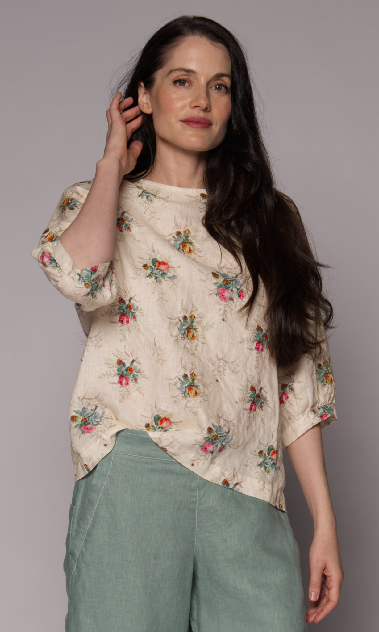Close-up of a dark-haired woman wearing a floral 3/4-sleeve top and light green pants.