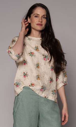 Close-up of a dark-haired woman wearing a floral 3/4-sleeve top and light green pants.