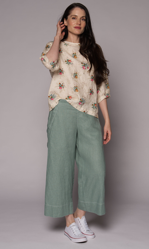 A dark-haired woman wearing a floral 3/4-sleeve top and light green pants.