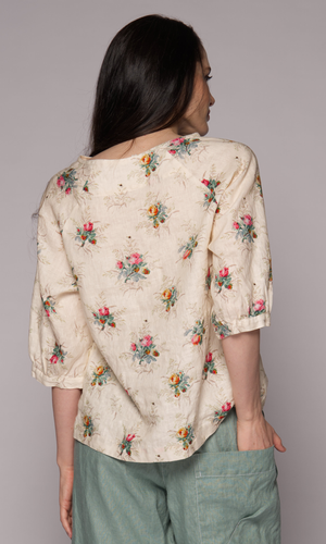 Close-up of the back of a dark-haired woman wearing a floral 3/4-sleeve top and light green pants.
