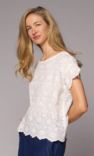 Blonde haired woman modelling a white lace top, with denim pants.