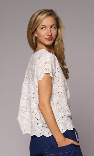Blonde haired woman modelling a white lace top, with denim pants, hand in pocket.