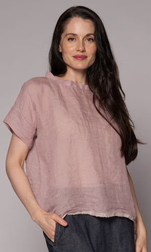 Dark brown haired woman modelling a light pink linen top and denim skirt with hand in pocket.