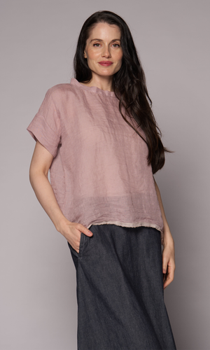 Dark brown haired woman modelling a light pink linen top and denim skirt with hand in pocket.