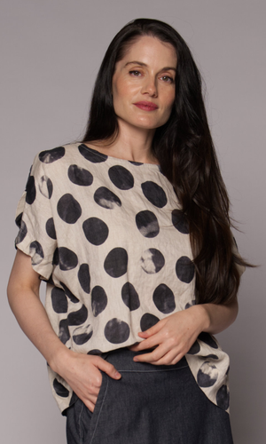 Close up of a woman models a top with a black-and-white abstract polka-dot pattern, paired with a dark denim skirt.