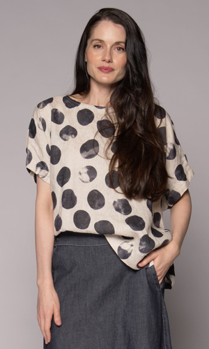 A woman models a top with a black-and-white abstract polka-dot pattern, paired with a dark denim skirt.