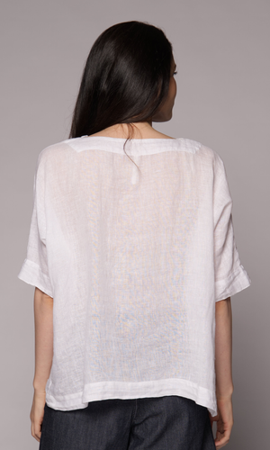 Brown-haired woman modelling a white linen top and denim shorts, showing us the back of the top.