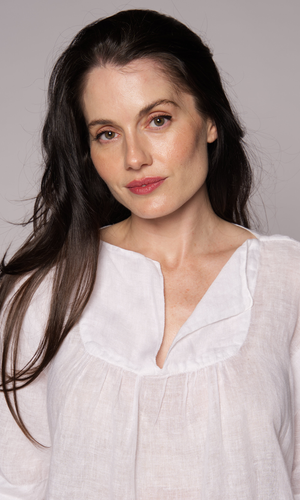 Close-up of a brown-haired woman modelling the neckline of a white linen top.