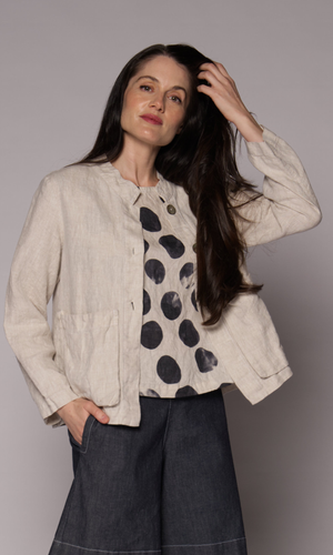 A woman models a cream coloured jacket with a black-and-white abstract polka-dot patterned top, paired with a dark denim wide leg shorts