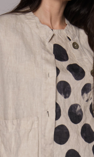 Closeup of the round neckline on a cream coloured jacket with a black-and-white abstract polka-dot patterned top.