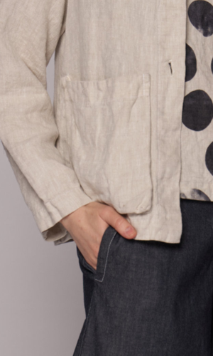Closeup of the rectangular pocket on a cream coloured jacket with a black-and-white abstract polka-dot patterned top, with model's hand in the denim short's pocket.