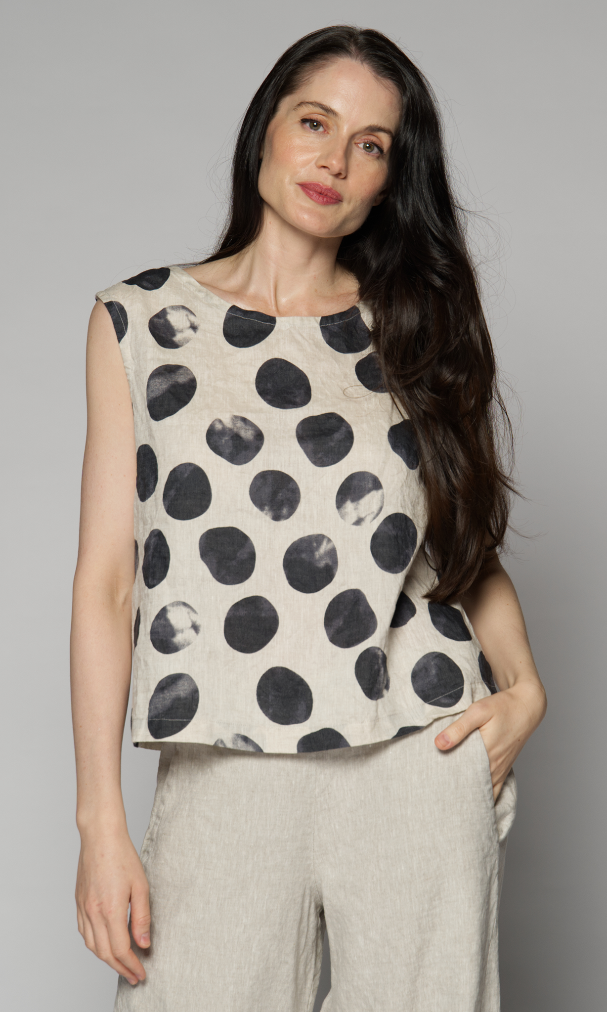 Lady with dark brown hair, wearing a sleeveless dotted top, in cream and black.