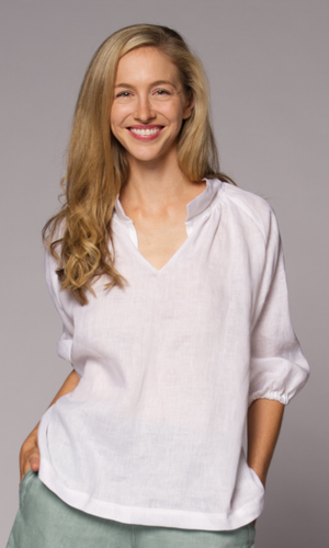 Close-up of a blonde woman wearing a white collared top and denim pants.