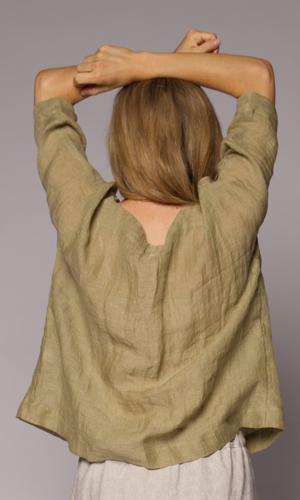 Blonde-haired woman modelling a light green linen top , showing us the back of the top.