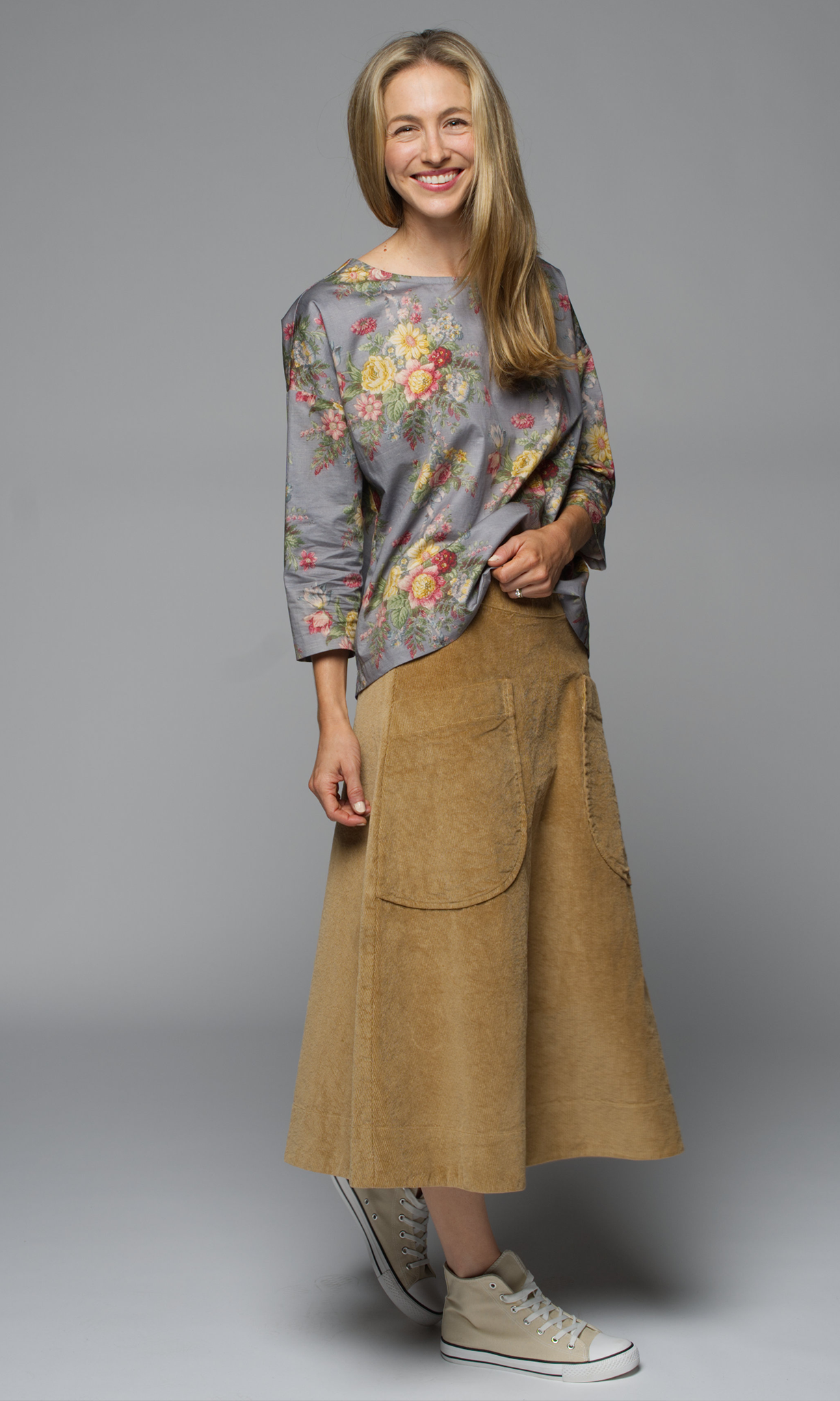 A women wearing a floral top with a camel coloured skirt.