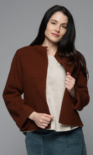 A woman in a rust coloured jacket with a white top and blue shirt.