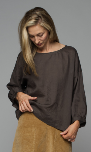 A woman wearing a dark brown blouse and beige skirt.