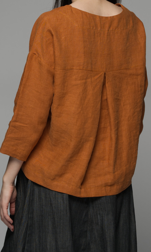 A woman wears a long sleeve rust coloured top and dark blue pants, showing up the back of the top and neckline.