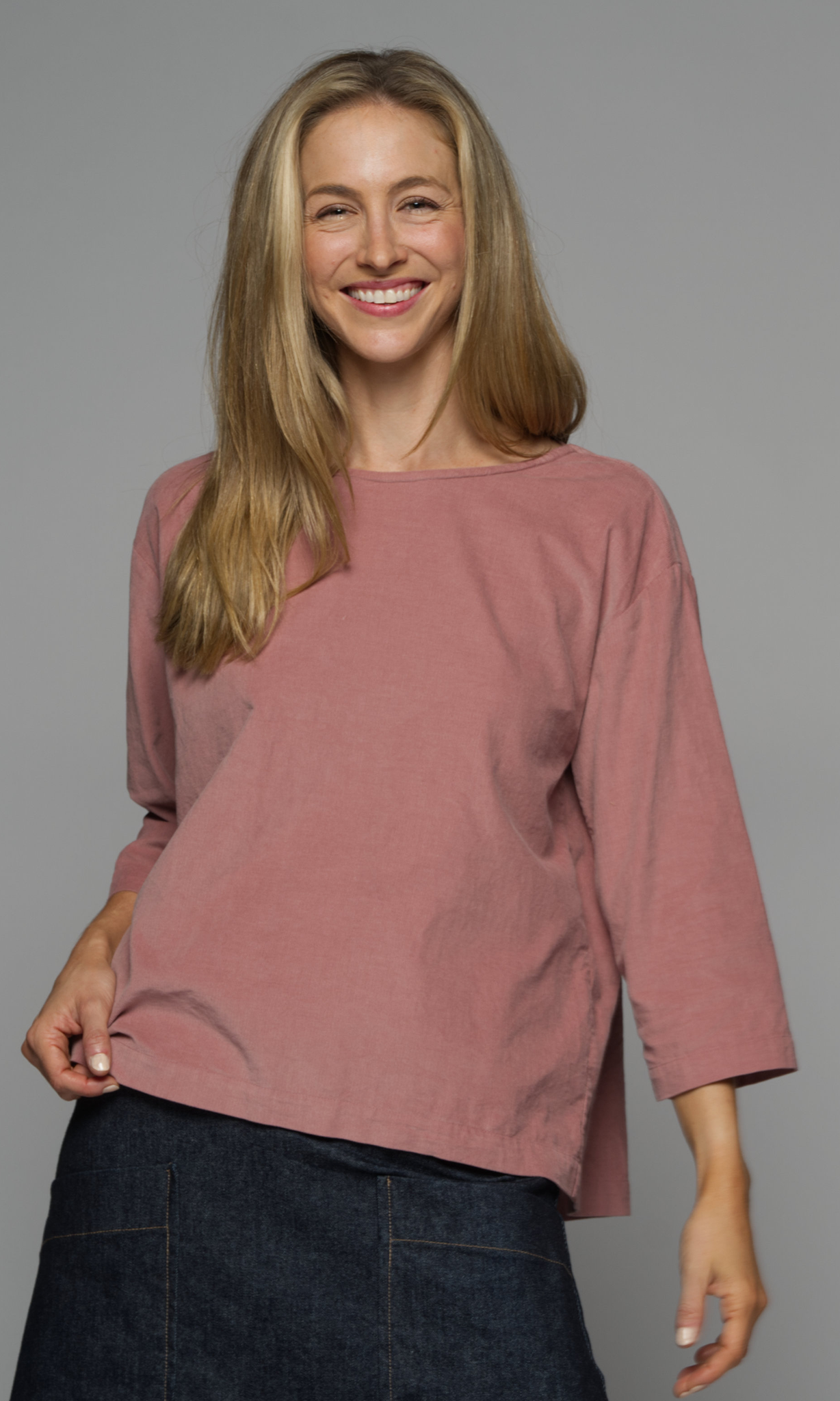 A woman wearing a pink long sleeved top with a denim skirt.