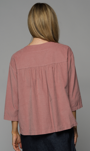 A woman wearing a pink long sleeved top with a denim skirt, showing the back of the top.