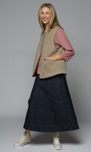 A woman wearing a beige vest over a pink shirt with a long dark blue skirt.