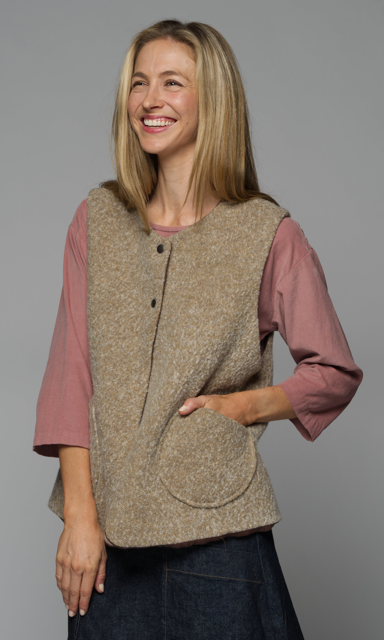 A woman wearing a beige vest over a pink shirt and a denim skirt.