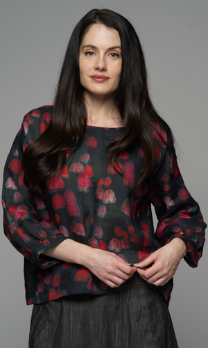 A woman wearing a dark blouse with a red floral pattern.