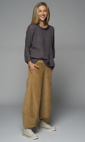 A women wearing a grey top and camel corduroy pants with hand in pocket.