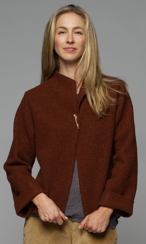 A woman in a rust coloured jacket with a grey top and beige corduroy pants.