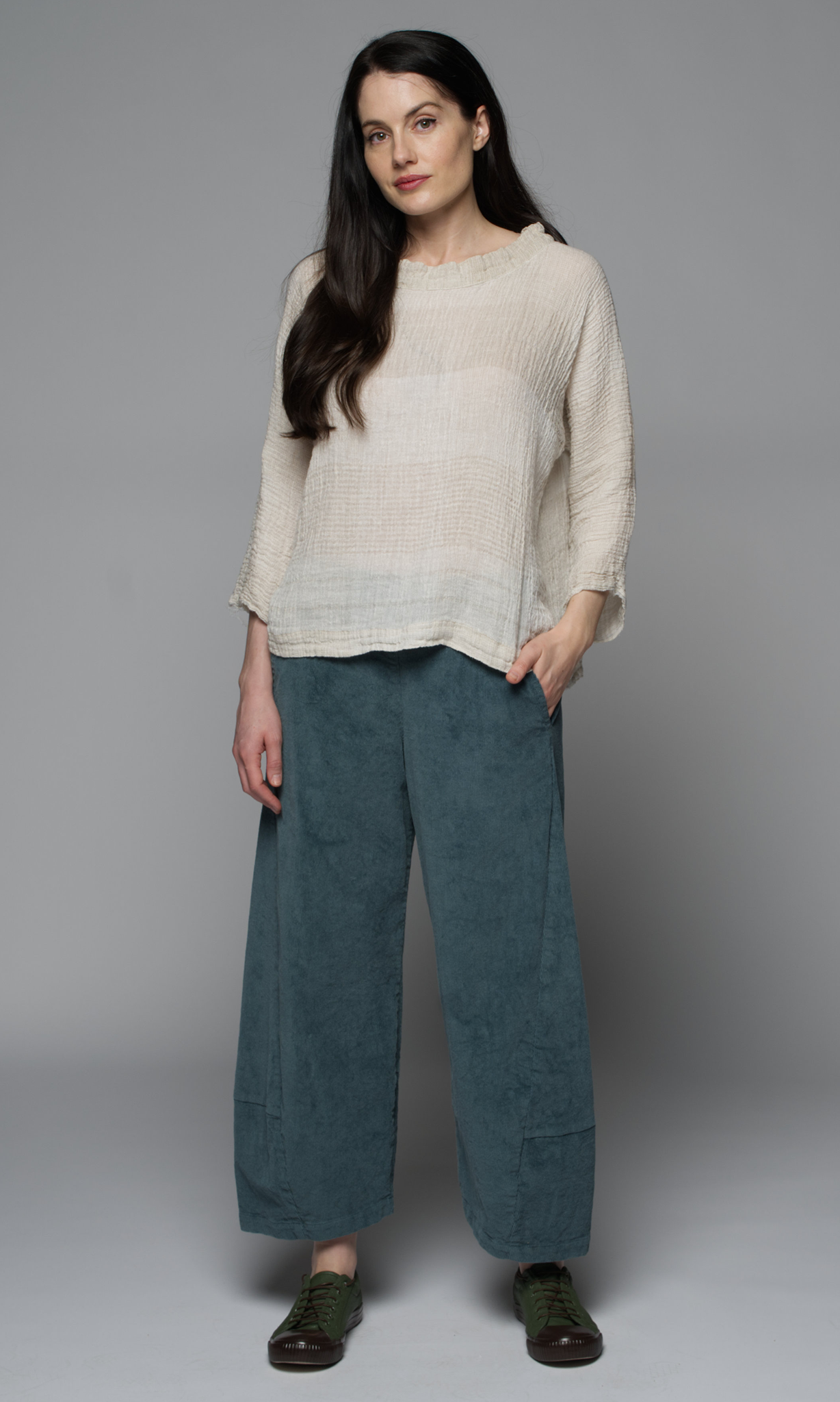 A woman wearing a beige top and teal pants.