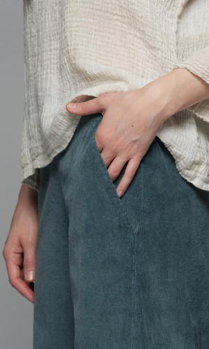 Person wearing a beige textured shirt and teal pants.