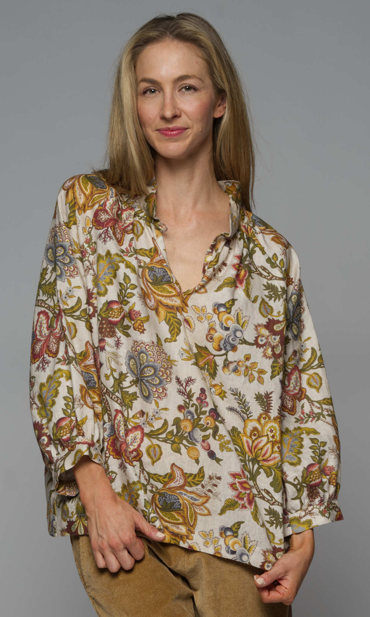 A woman wearing a long sleeve top with a floral pattern and corduroy beige pants.