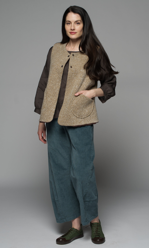 A woman wearing a beige jacket and teal pants.