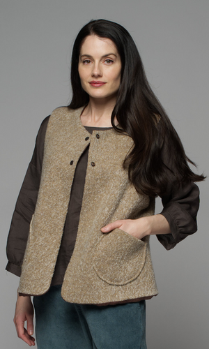A woman wearing a beige vest over a long brown shirt and a mid-blue corduroy pants.