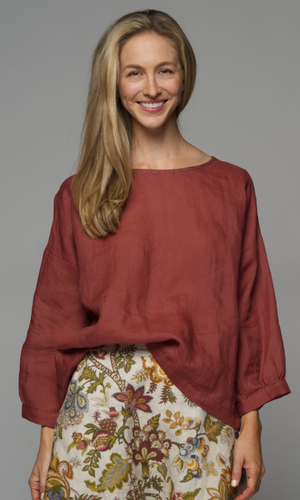 A woman wearing a rust coloured blouse with a floral skirt.