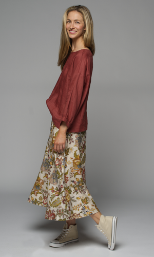 A woman wearing a rust coloured top and a floral skirt.